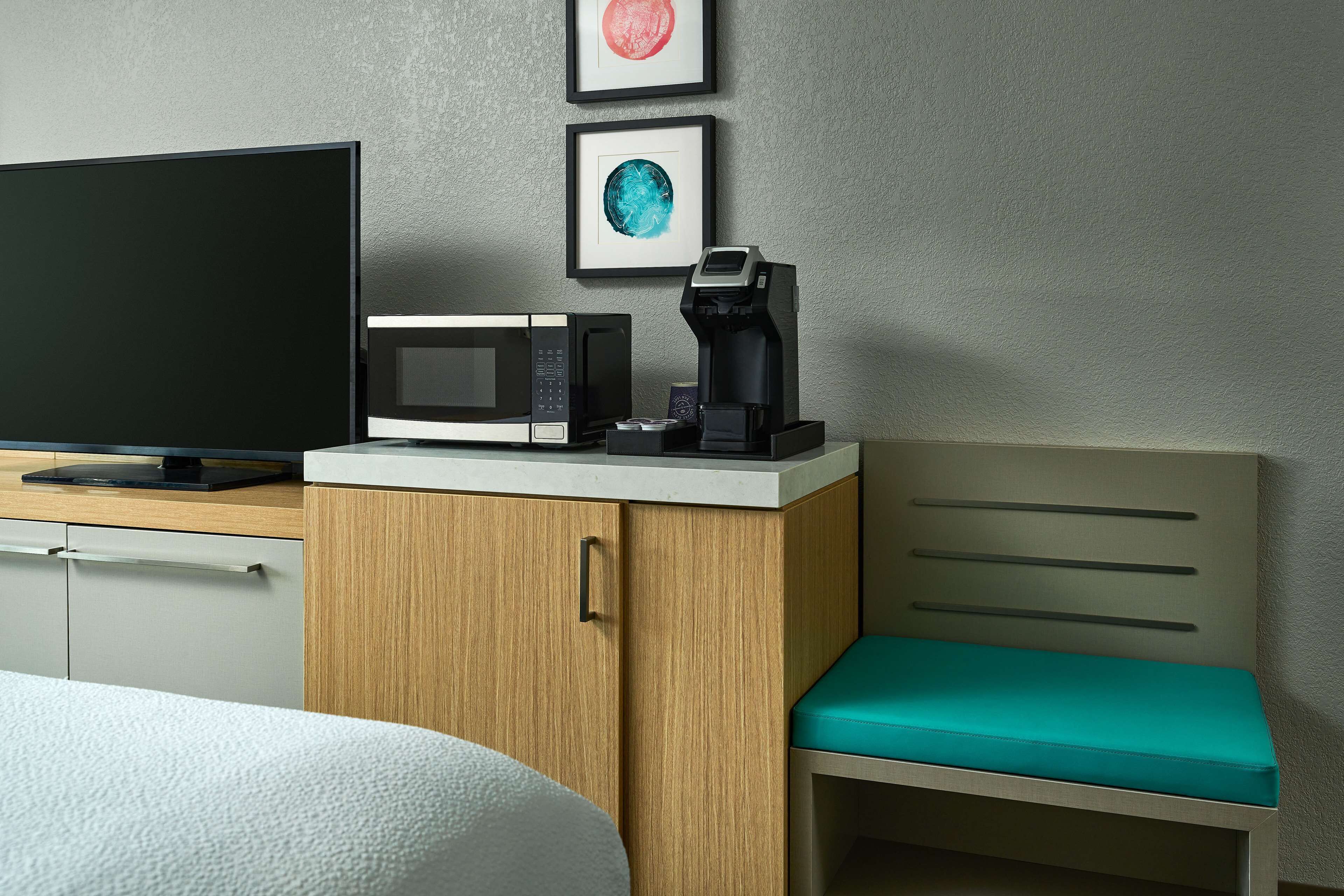 A hotel room with a bed, a TV, a microwave, a coffee maker, and a wooden cabinet.