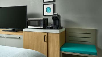 A hotel room with a bed, a TV, a microwave, a coffee maker, and a wooden cabinet.