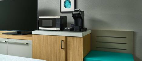 Una habitación de hotel con cama, televisión, microondas, cafetera y un mueble de madera.