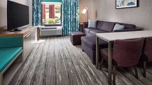 A modern hotel room with a flat-screen TV, a sofa, a dining table, and a large window with curtains. - Hilton Garden Inn Tewksbury Andover (Tewksbury)