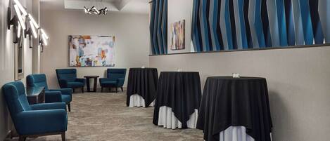 Une salle de conférence avec des chaises bleues, des tables recouvertes de nappes noires, des œuvres d’art abstrait aux murs et un luminaire au plafond.