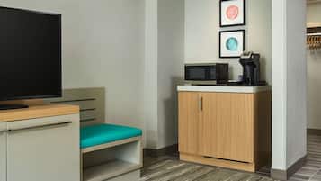 Ein Hotelzimmer mit Fernseher, Mikrowelle, Kaffeemaschine, einer türkisblauen Bank und einem Holzkabinent.