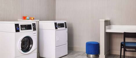 A laundry room with two white washing machines, a blue stool, and a chair.