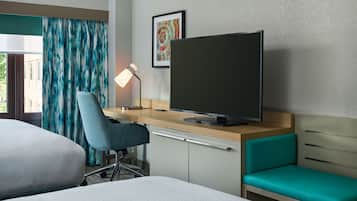 Habitación de hotel con cama, escritorio, computadora, silla, televisor y un pequeño sofá.