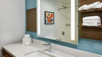 Un baño con un espejo grande, un lavabo, un perchero para toallas y un cuadro en la pared.