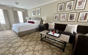 A hotel room with a large bed, a dark brown sofa, a coffee table with wine glasses, and framed artwork on the walls. - The Henley Park Hotel (Washington)