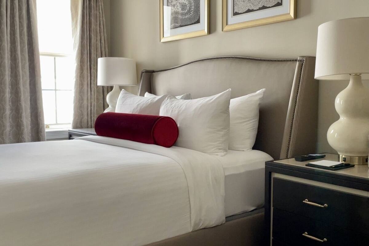 A hotel room with a bed, two bedside lamps, a nightstand, and a drawer.