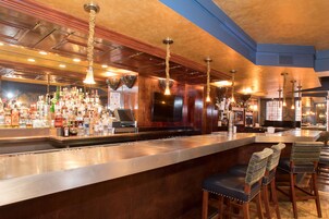 Un bar con una barra alargada, varias luces colgantes y una amplia variedad de botellas.
