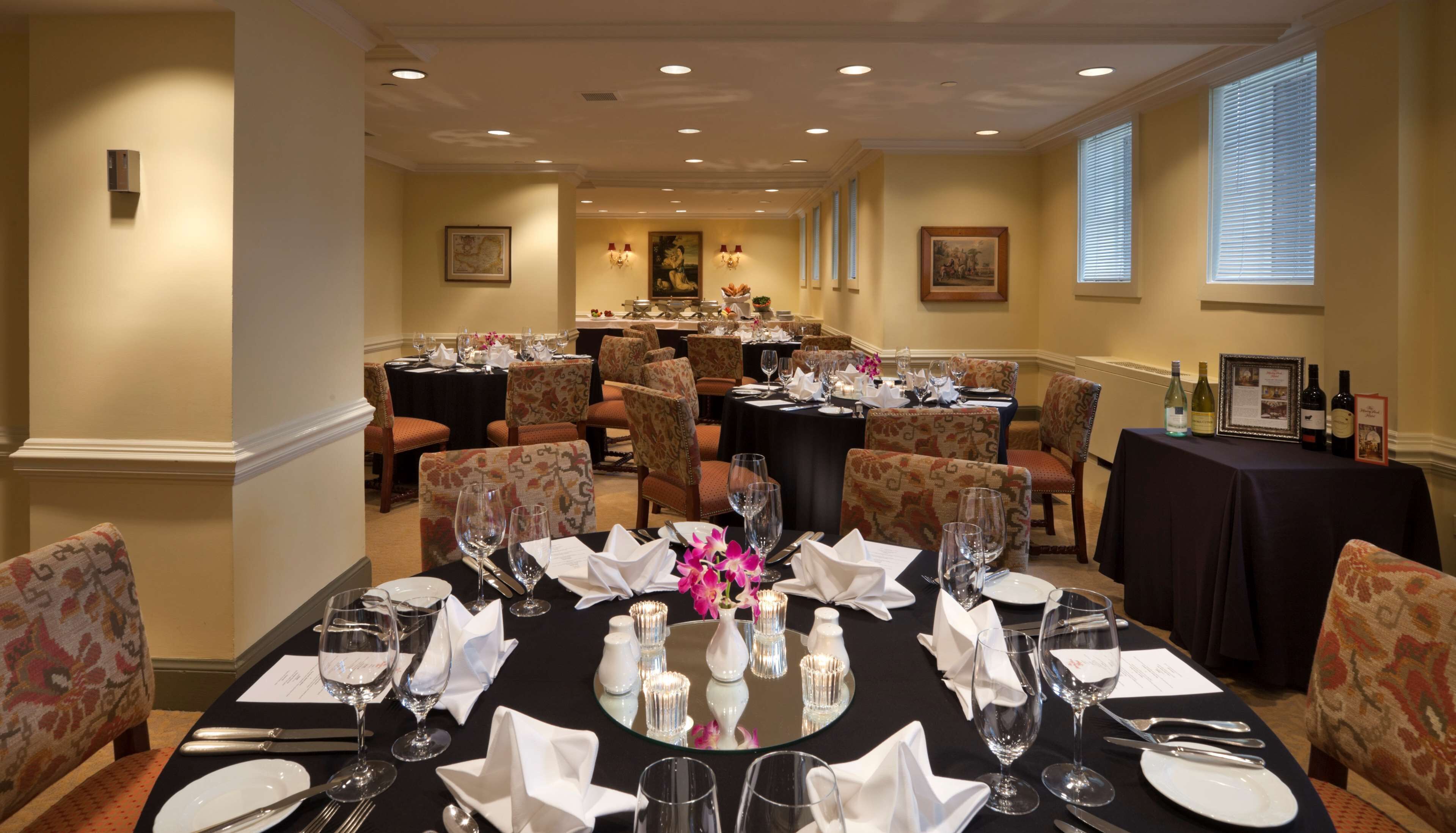 A formal dining room with multiple tables set for a meal, featuring chairs, wine glasses, and a central floral arrangement.