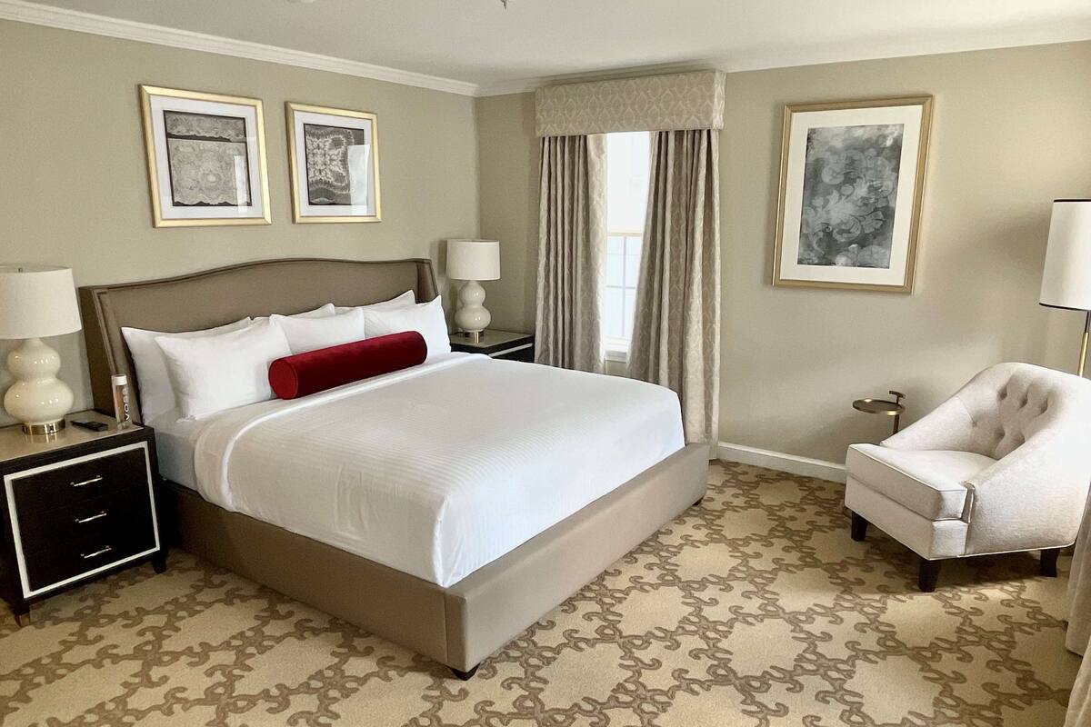 A neatly arranged hotel room with a large bed, a chair, a nightstand, and two framed pictures on the wall.