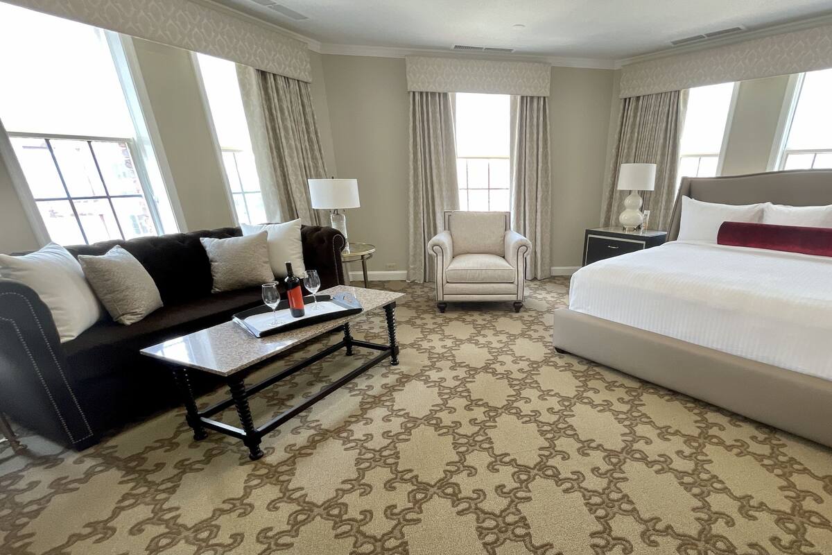 A hotel room with a large bed, a sofa, a chair, and a small table with a bottle and glasses.