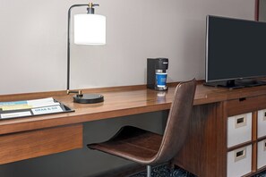 Un bureau d’hôtel équipé d’une machine à café, d’une lampe, d’un écran d’ordinateur et d’une chaise.
