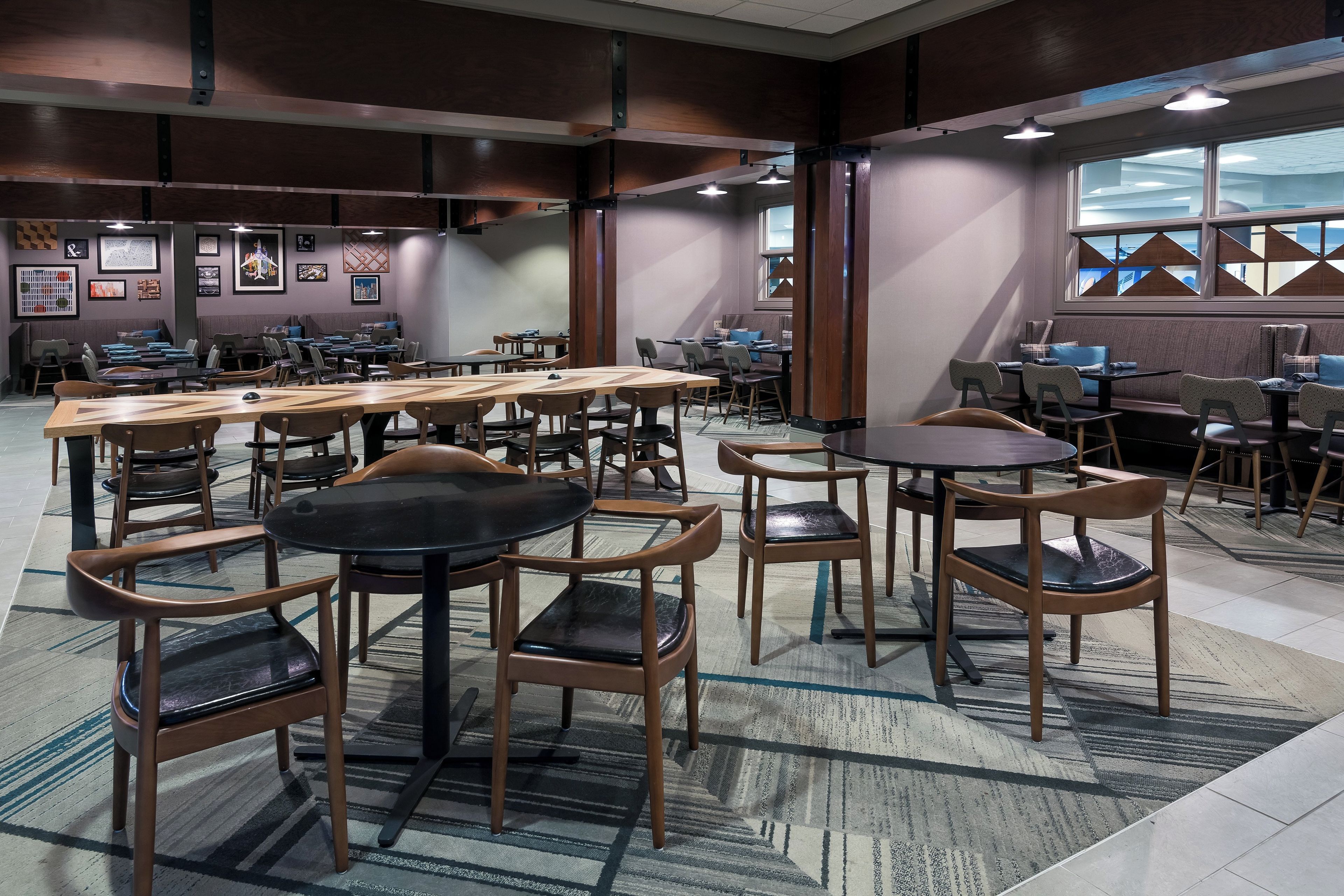 A spacious dining area with multiple tables and chairs, a patterned carpet, and framed artwork on the walls.