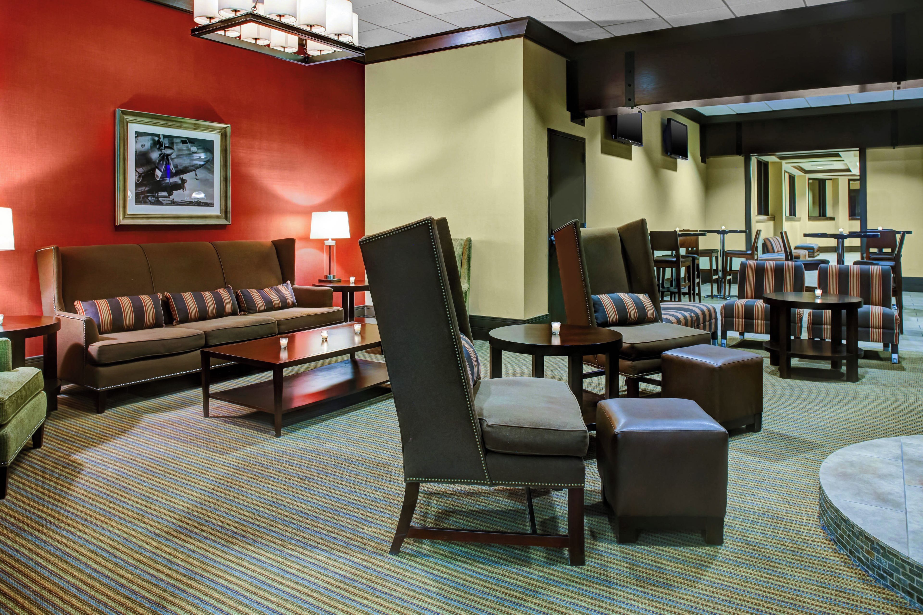 A hotel lobby with a red wall, a sofa set, a coffee table, a chair, and a dining area with tables and chairs.