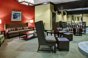 Un hall de hotel con una pared roja, un conjunto de sofás, una mesa de centro, una silla y una zona de comedor con mesas y sillas.
