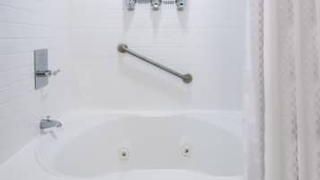 A white bathtub with a grab bar, a handheld showerhead, and a wall-mounted faucet.