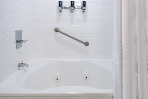 Une baignoire blanche équipée d’une barre d’appui, d’un pommeau de douche à main et d’un robinet mural.