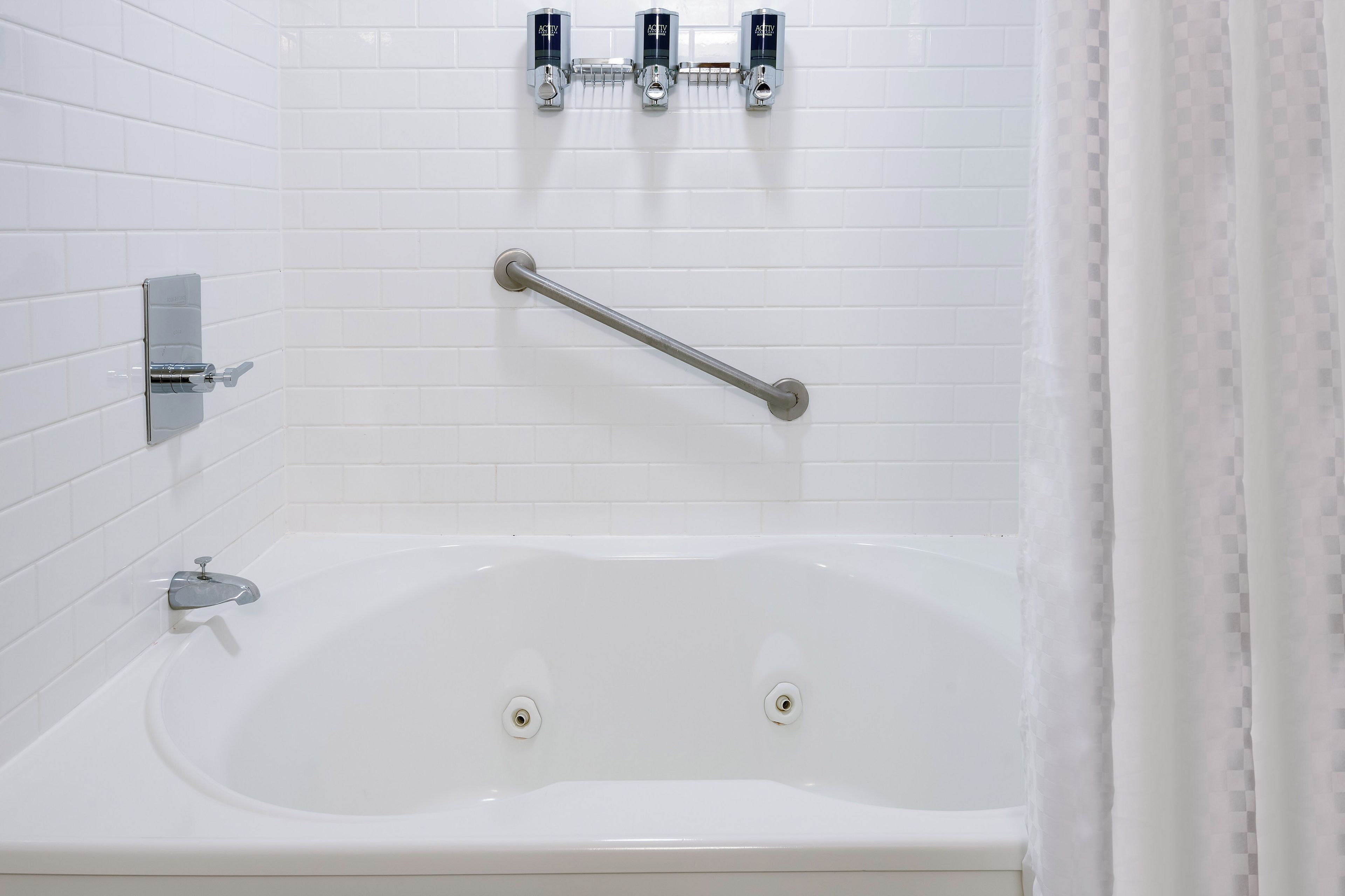 A white bathtub with a grab bar, a handheld showerhead, and a wall-mounted faucet.