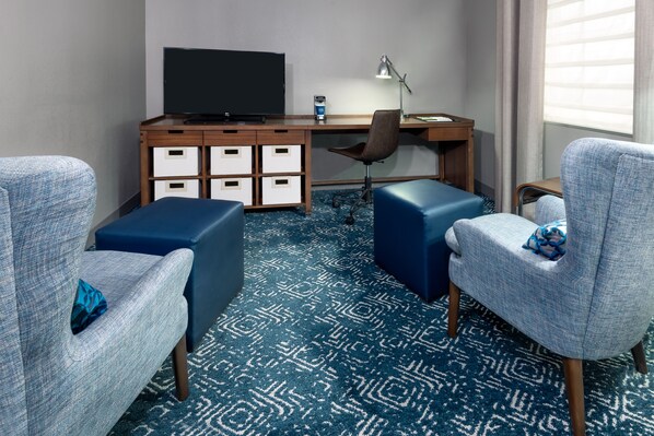 Habitación de hotel con cama, escritorio con televisor de pantalla plana, silla, lámpara y alfombra azul estampada.