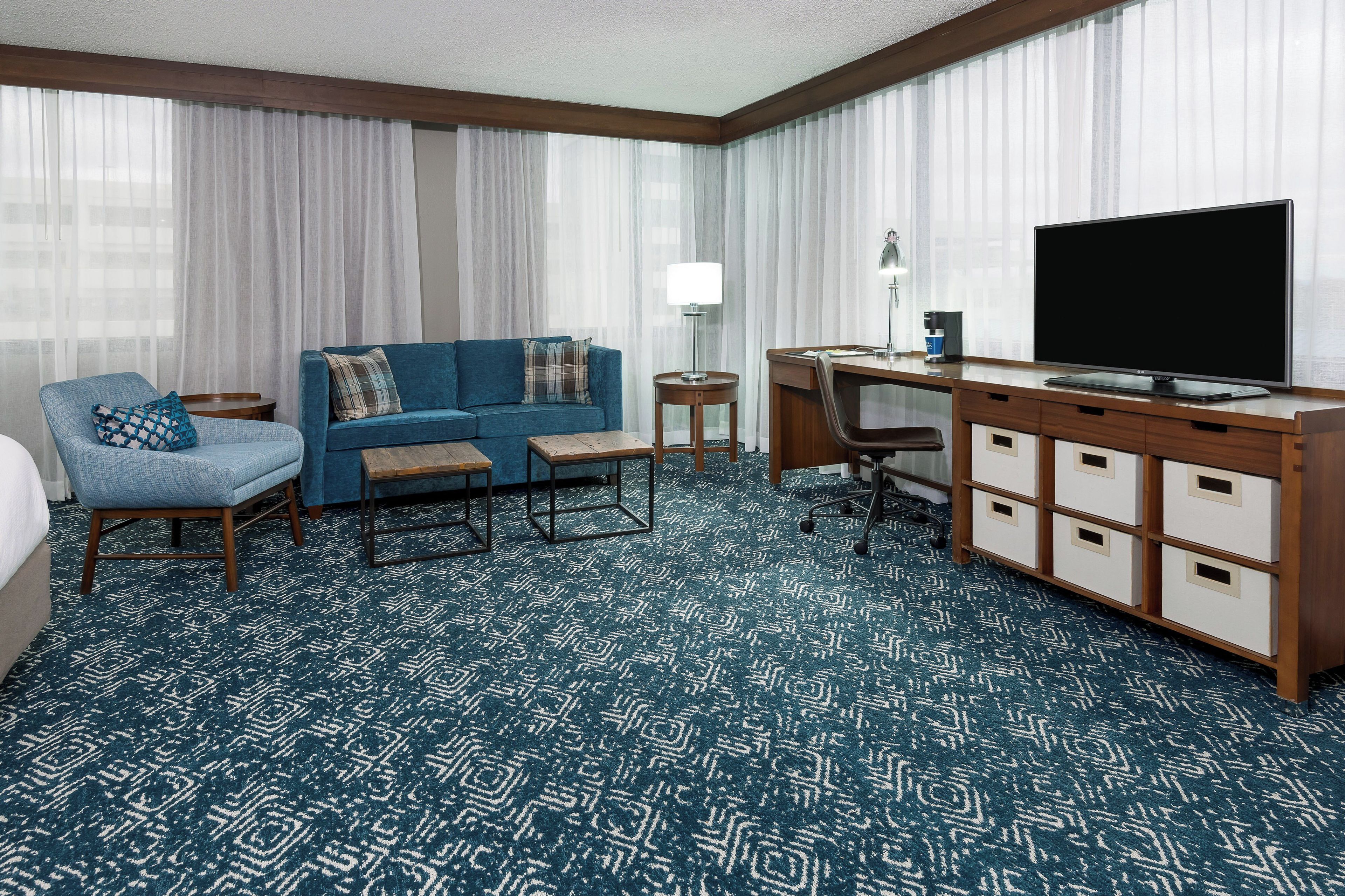 Une chambre d’hôtel avec un canapé bleu, un bureau avec un ordinateur, une télévision et un minibar.