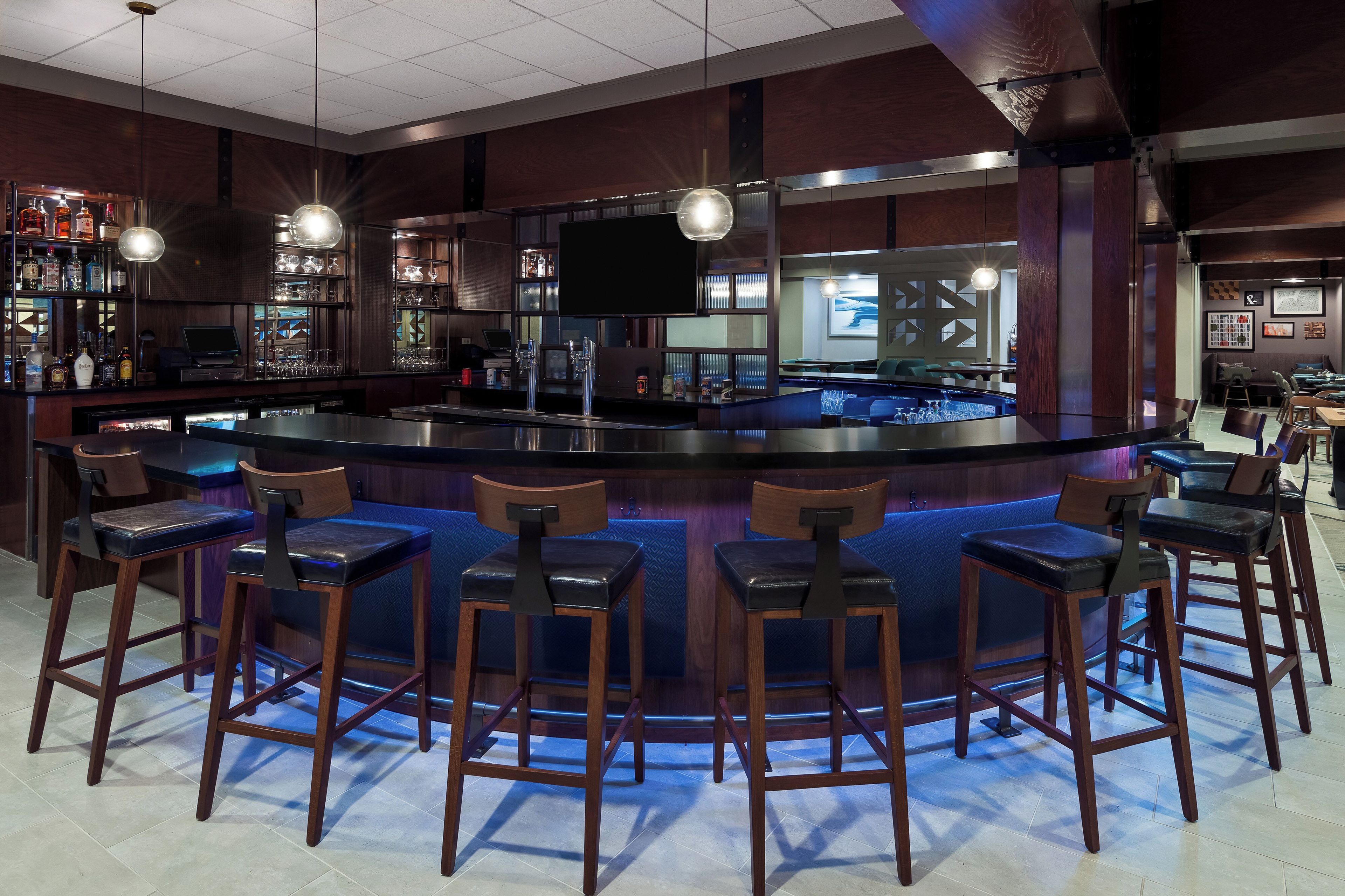 A bar area with a counter, stools, and a television screen.