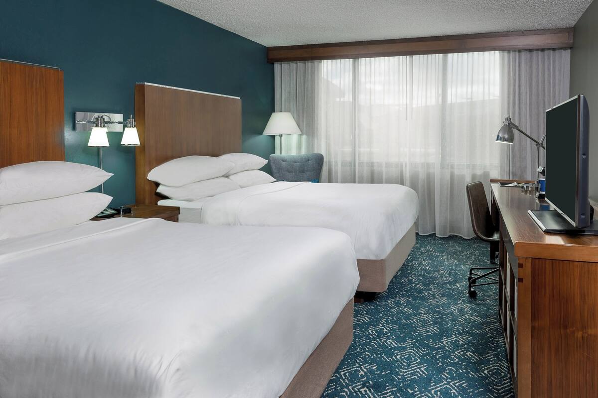 A hotel room with two beds, a desk with a computer, a chair, a lamp, and a television.