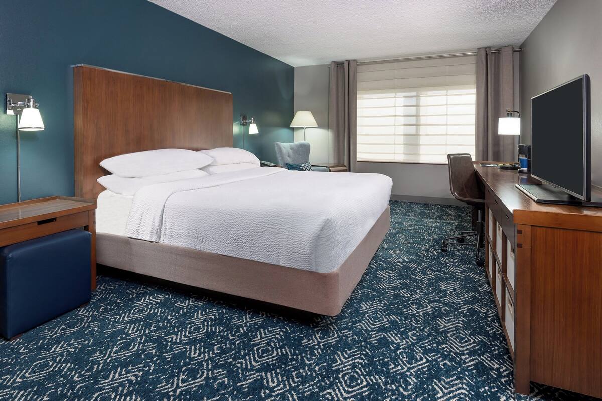 A hotel room with a large bed, a desk, a chair, a TV, and a window with curtains.