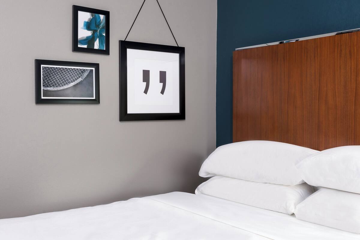 A neatly made bed with white linens, a wooden headboard, and three framed pictures on the wall.