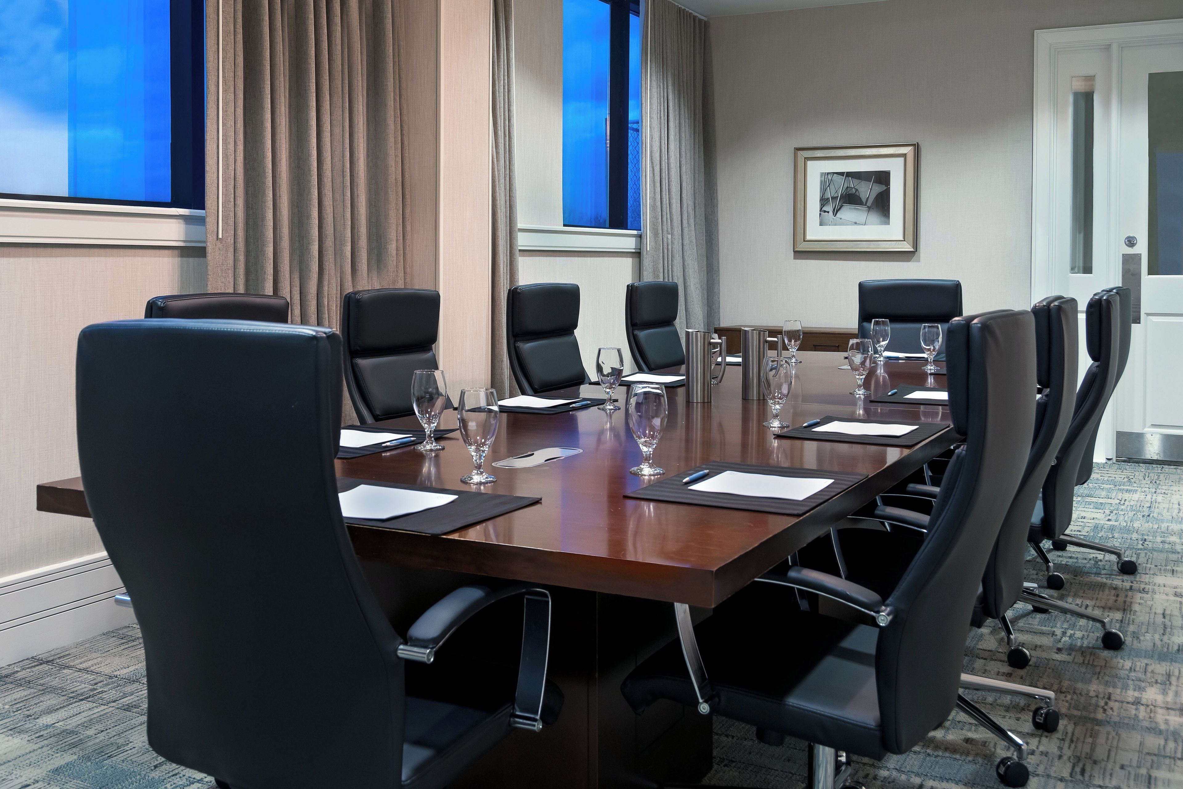 A conference room with a long table, six chairs, and six wine glasses.