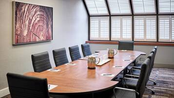 Un salón de conferencias con una mesa larga, seis sillas, un cuadro abstracto grande y una ventana con persianas.