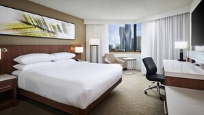 A hotel room with a large bed, a desk, a chair, a TV, and a view of tall buildings. - Delta Hotels by Marriott Toronto Mississauga (Mississauga)