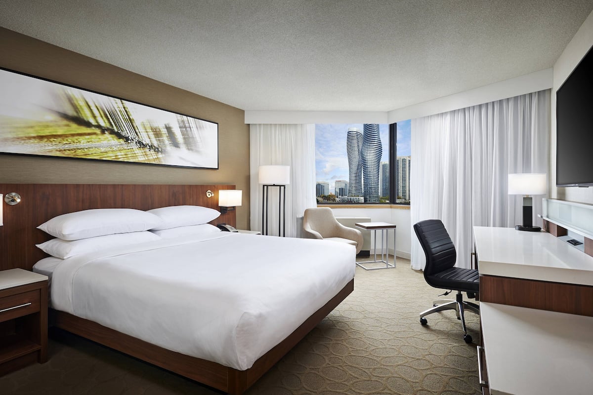 Habitación de hotel con una cama grande, un escritorio, una silla, un televisor y vistas a edificios altos.