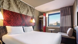 Habitación de hotel con una cama grande, una mesita, un sofá, vistas a la ciudad y una alfombra roja.