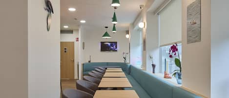 A modern restaurant with long wooden tables and green cushioned booths.