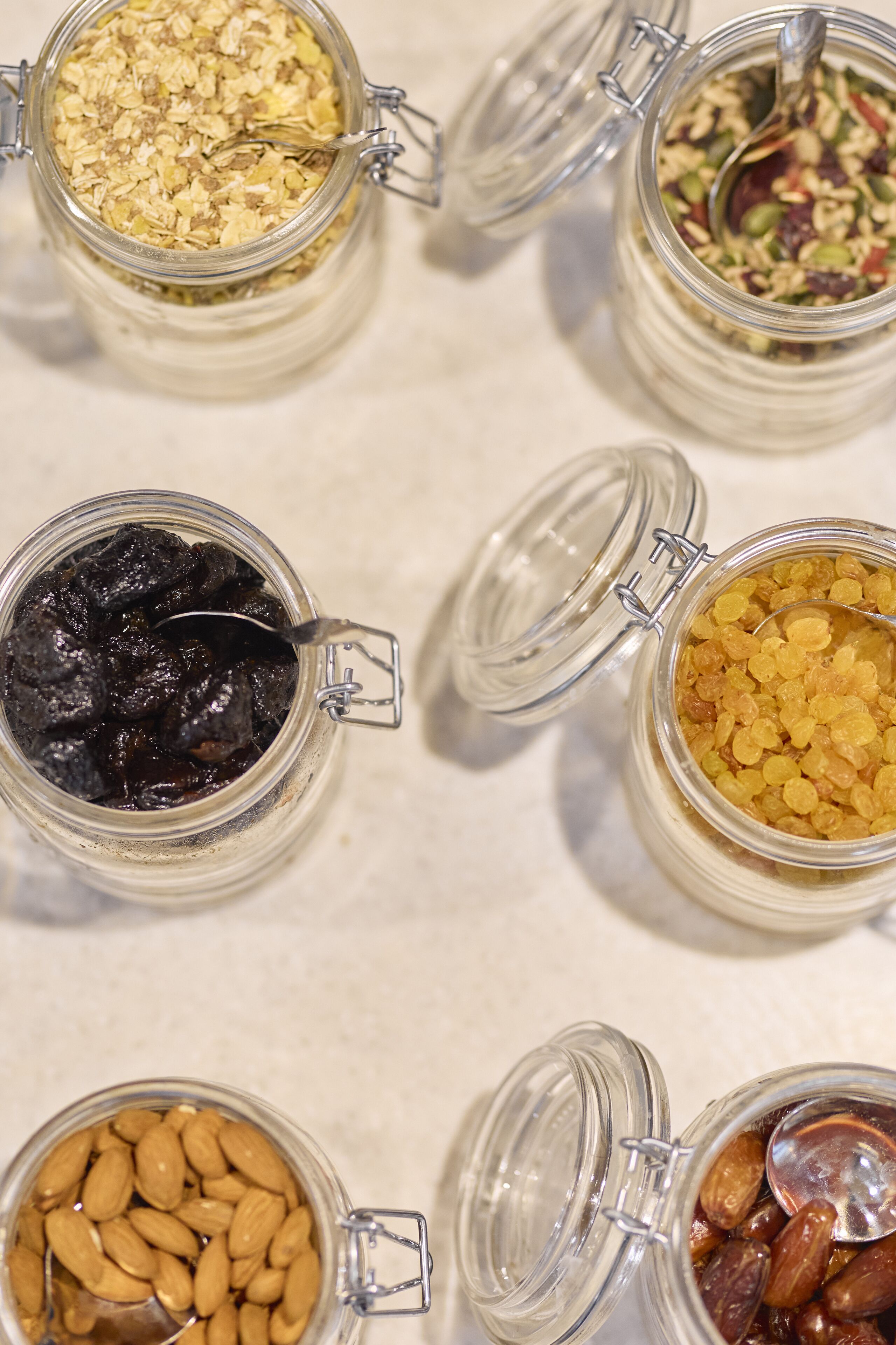 Cuatro frascos de vidrio con cierres metálicos, cada uno con distintos tipos de frutos secos y frutas deshidratadas.