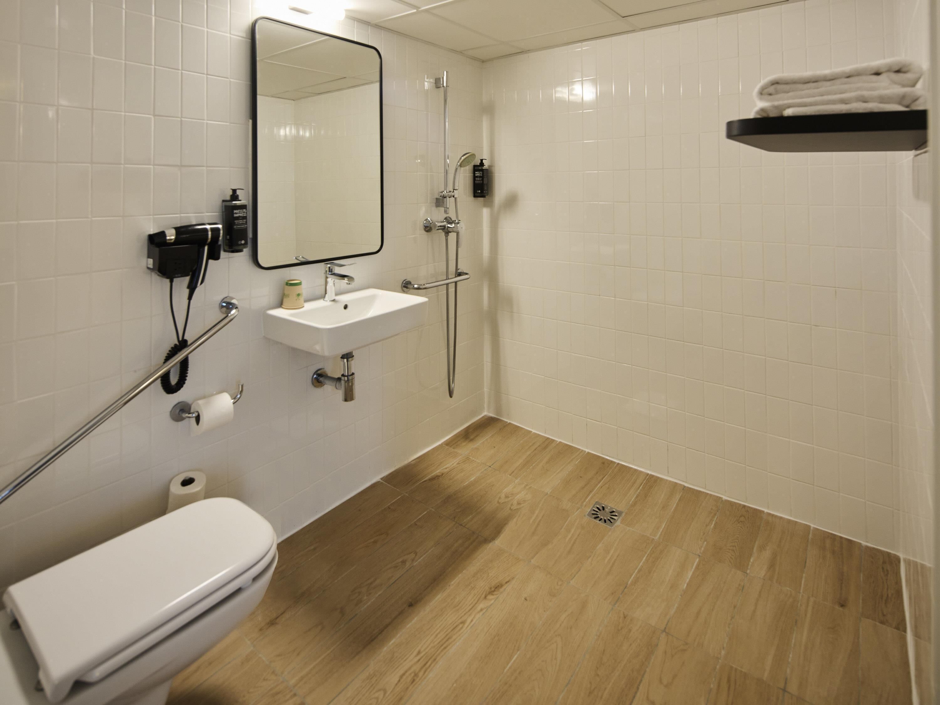 A bathroom with a toilet, sink, mirror, shower, and a towel rack.