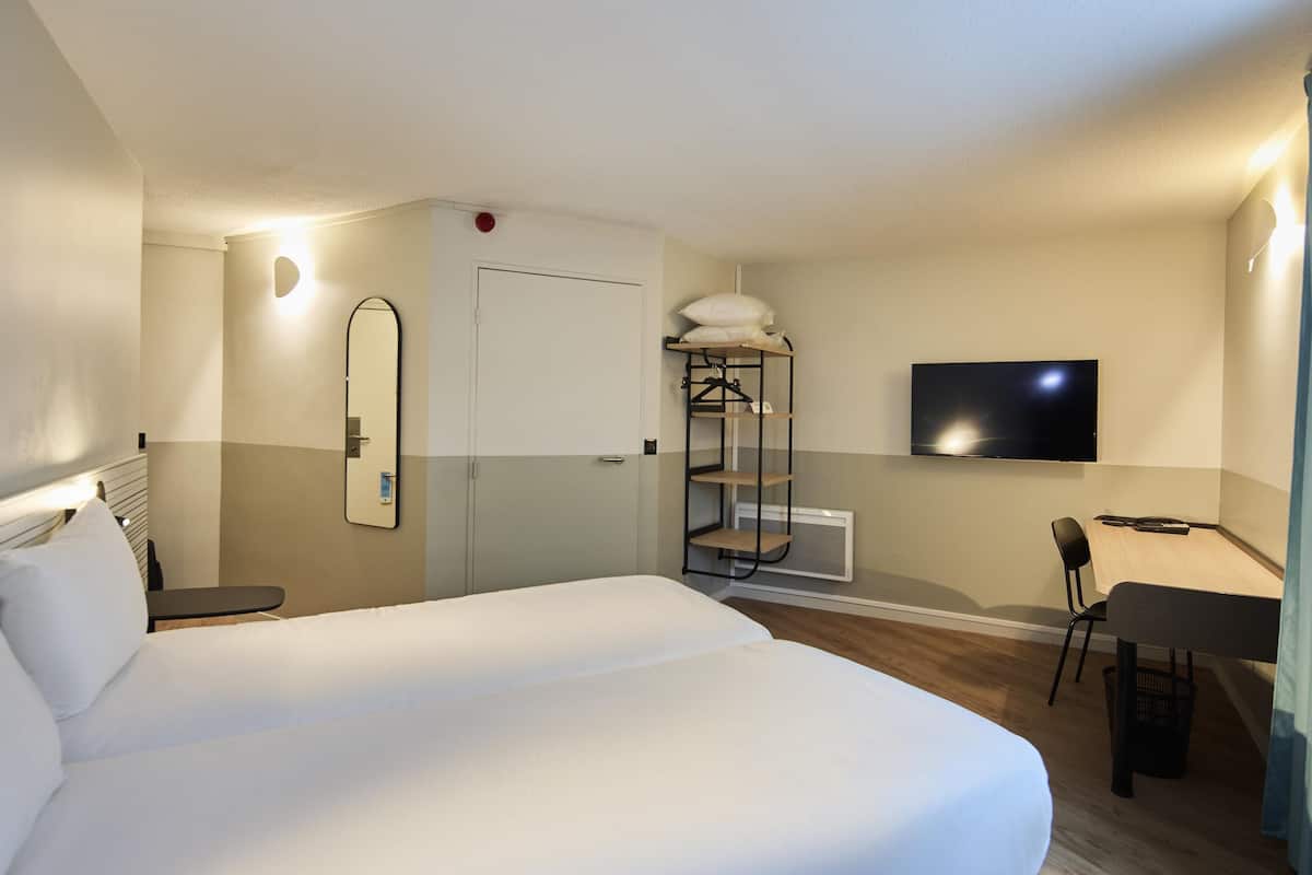 Une chambre d’hôtel avec un grand lit, un bureau avec une chaise, un téléviseur fixé au mur et une armoire.