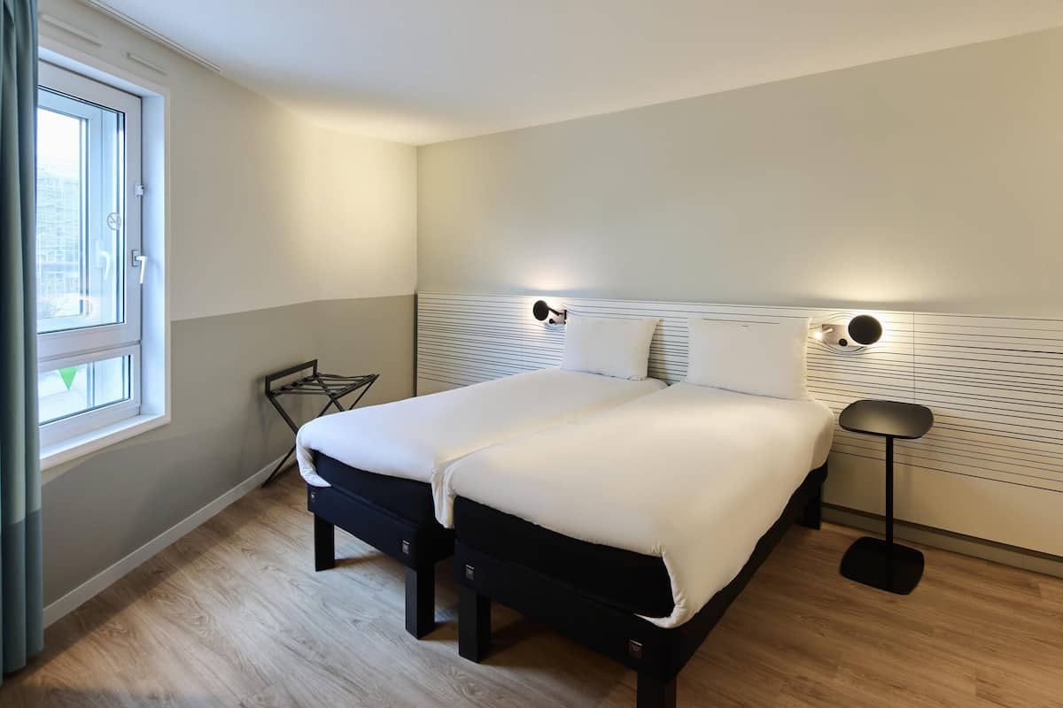 Un lit double avec une tête de lit, une table de chevet, une lampe et une fenêtre avec des rideaux.