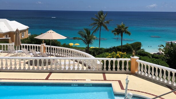 A pool area with a view of the ocean, palm trees, and a white balustrade.