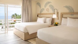 A hotel room with two beds, a balcony with a view of the ocean, and a tropical wall design.