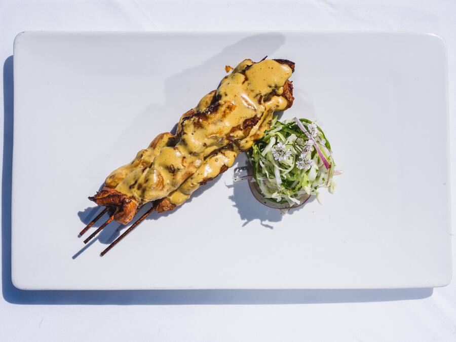 A white plate with a grilled meat skewer and a side salad.
