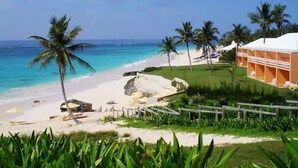 A beach resort with a white sandy beach, palm trees, and a building with a white roof.