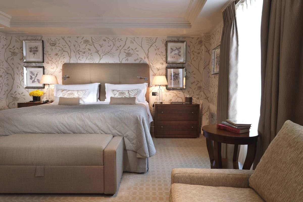 A hotel room with a large bed, two bedside tables with lamps, a wooden dresser, and a small table with books.