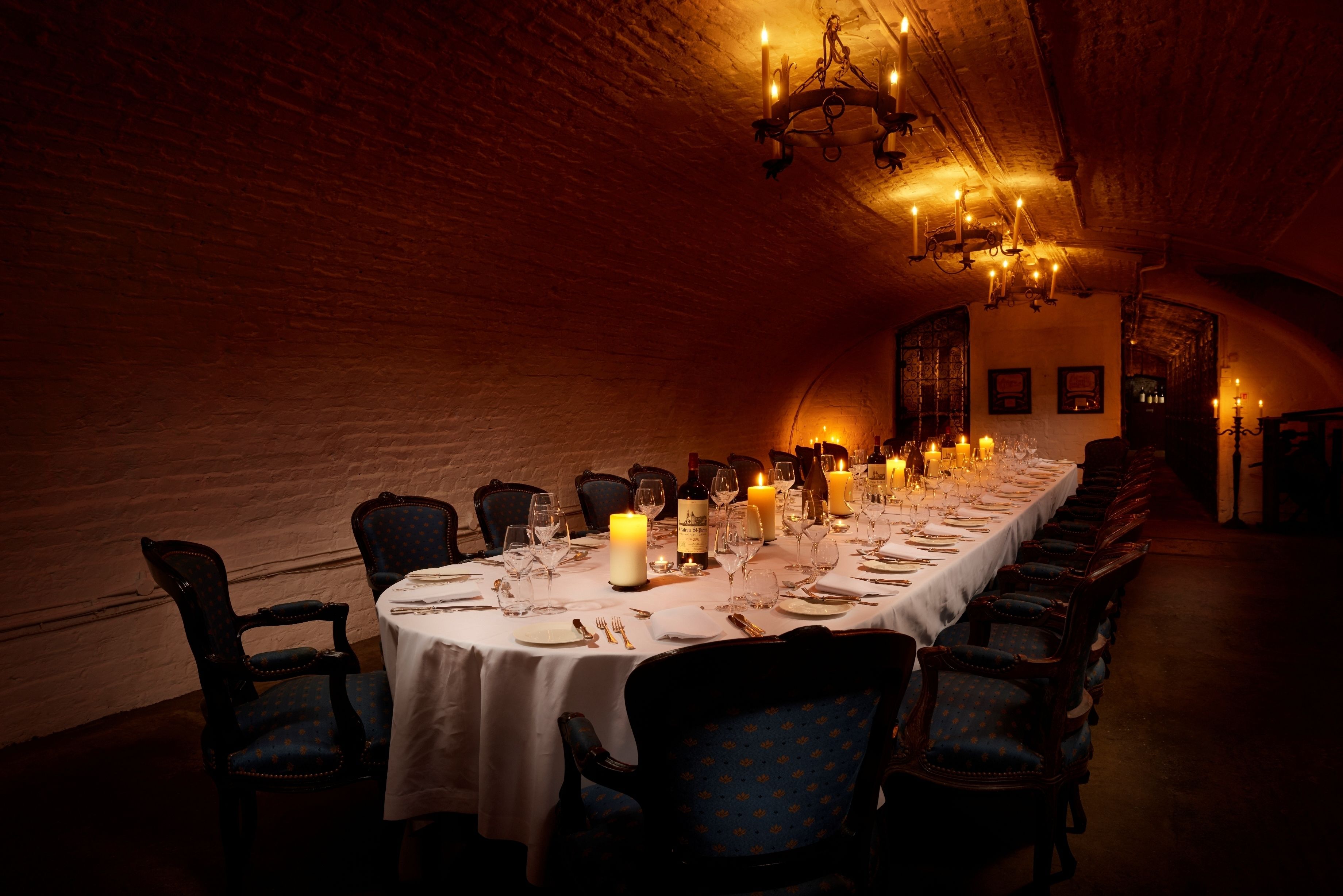 A long dining table set for a meal in a dimly lit room with brick walls and chandeliers.