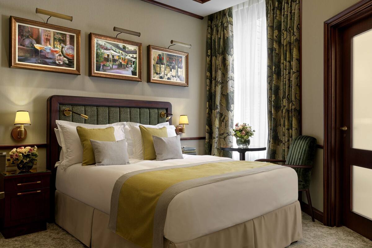 A hotel room with a large bed, two bedside tables with lamps, a chair, and three framed pictures on the wall.