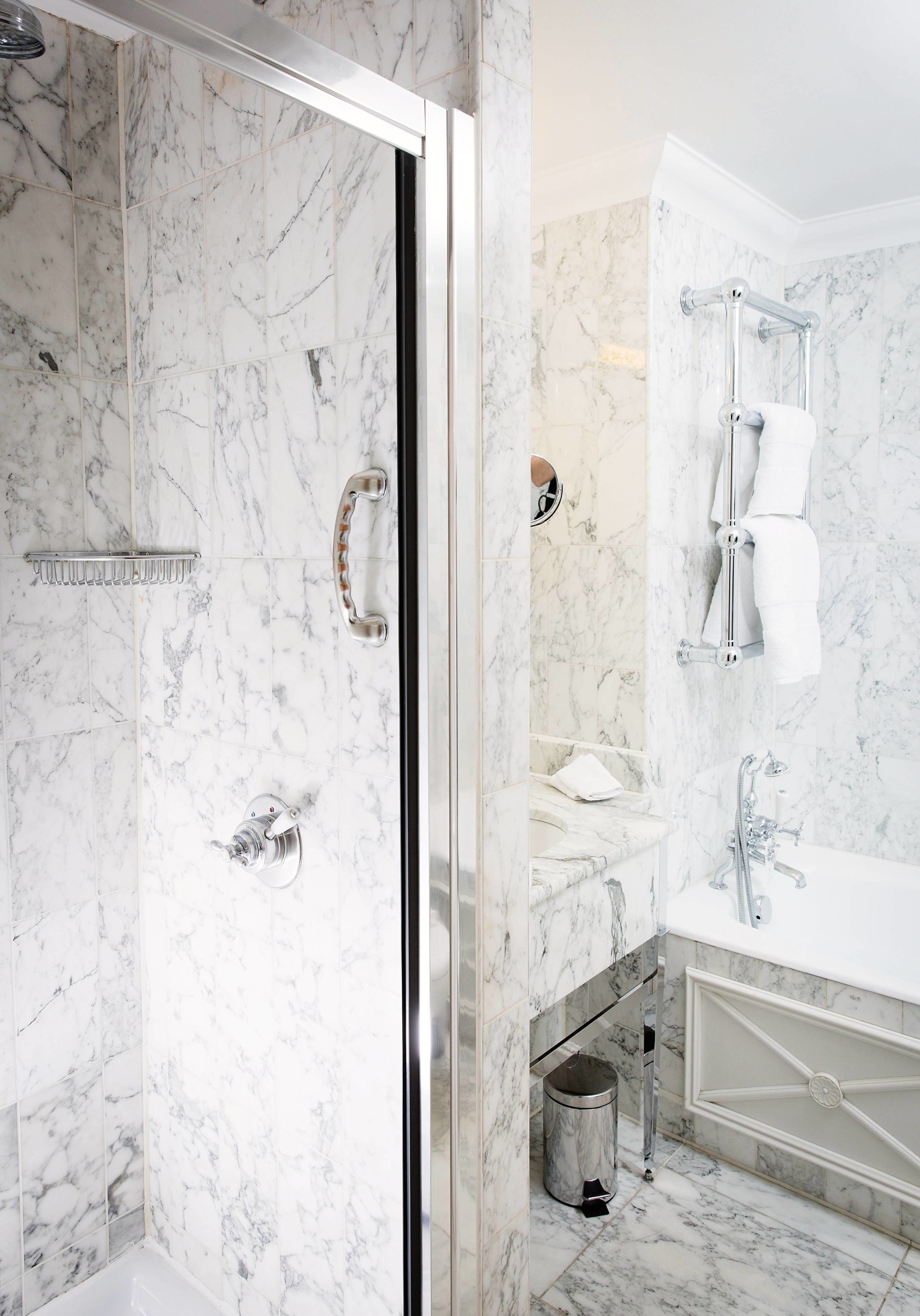 A modern bathroom with a glass-enclosed shower, a marble-tiled wall, a white sink with a chrome faucet, and a white bathtub.