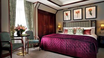 Ein Hotelzimmer mit einem großen Bett, zwei Stühlen, einem Tisch mit Blumenvase und gerahmten Bildern an der Wand.
