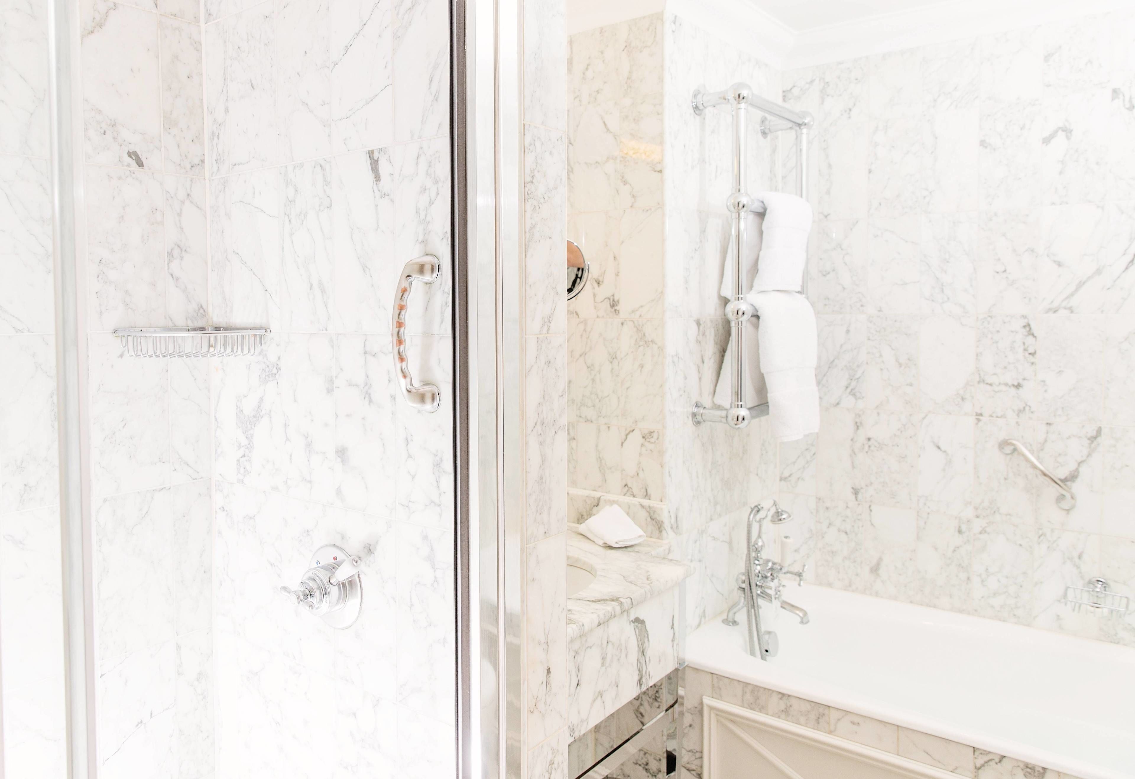 A bathroom with a glass-enclosed shower, marble walls, a white sink, and a towel rack.