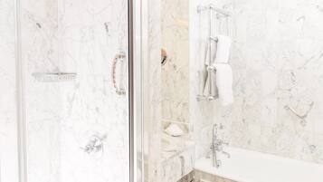 A bathroom with a glass-enclosed shower, marble walls, a white sink, and a towel rack.