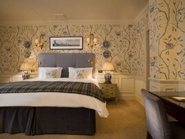 Ein Schlafzimmer mit einem großen Bett, zwei Nachttischen mit Lampen, einem Sessel und blumigem Wandpapier.